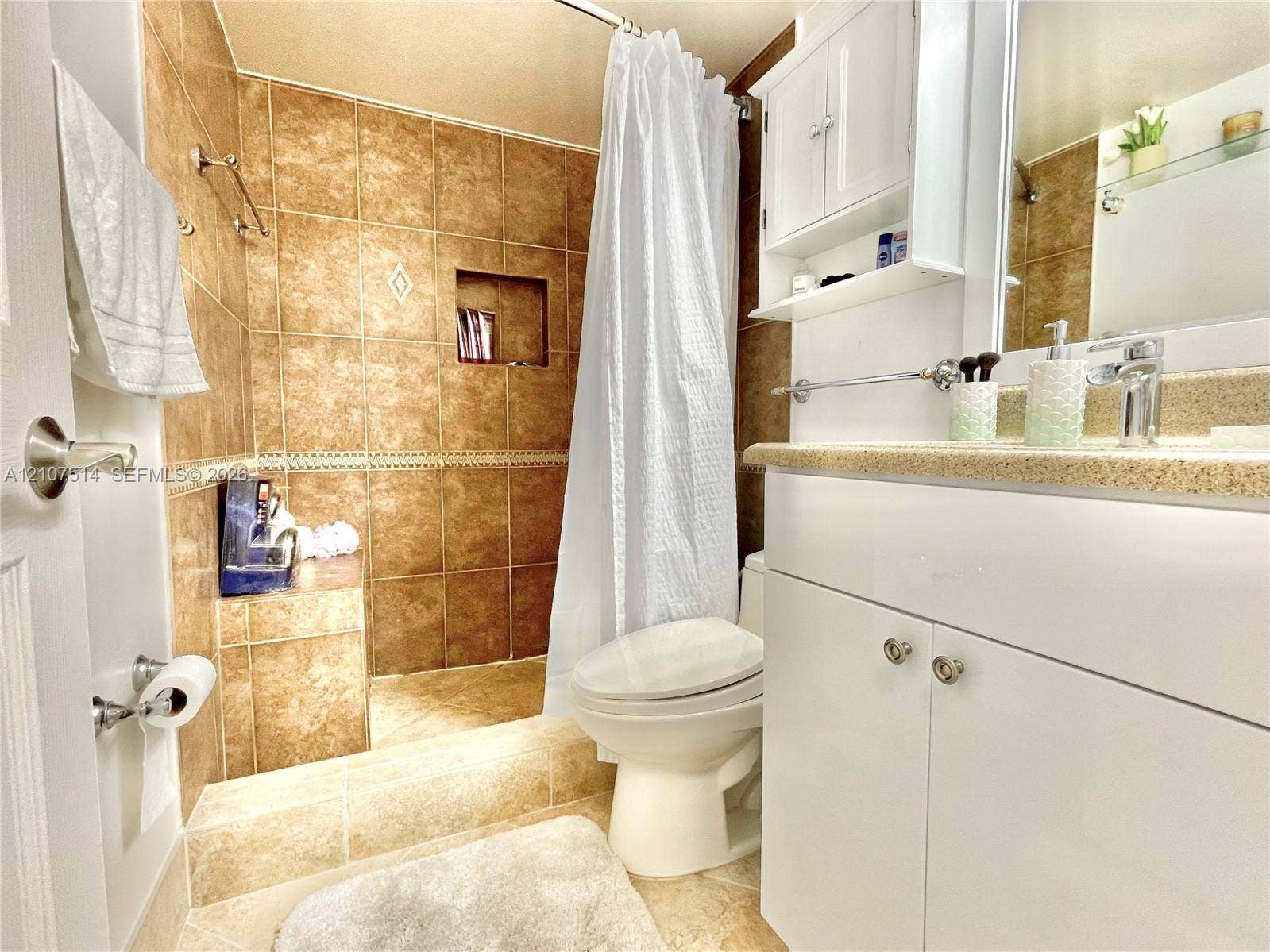 2750 NE 183rd Street, #2310, Aventura, Aventura, FL 33160 Bathroom featuring large-format tan wall tiles, built-in tiled shower bench with inset shelving, white vanity cabinetry with integrated countertop, and mounted medicine cabinet