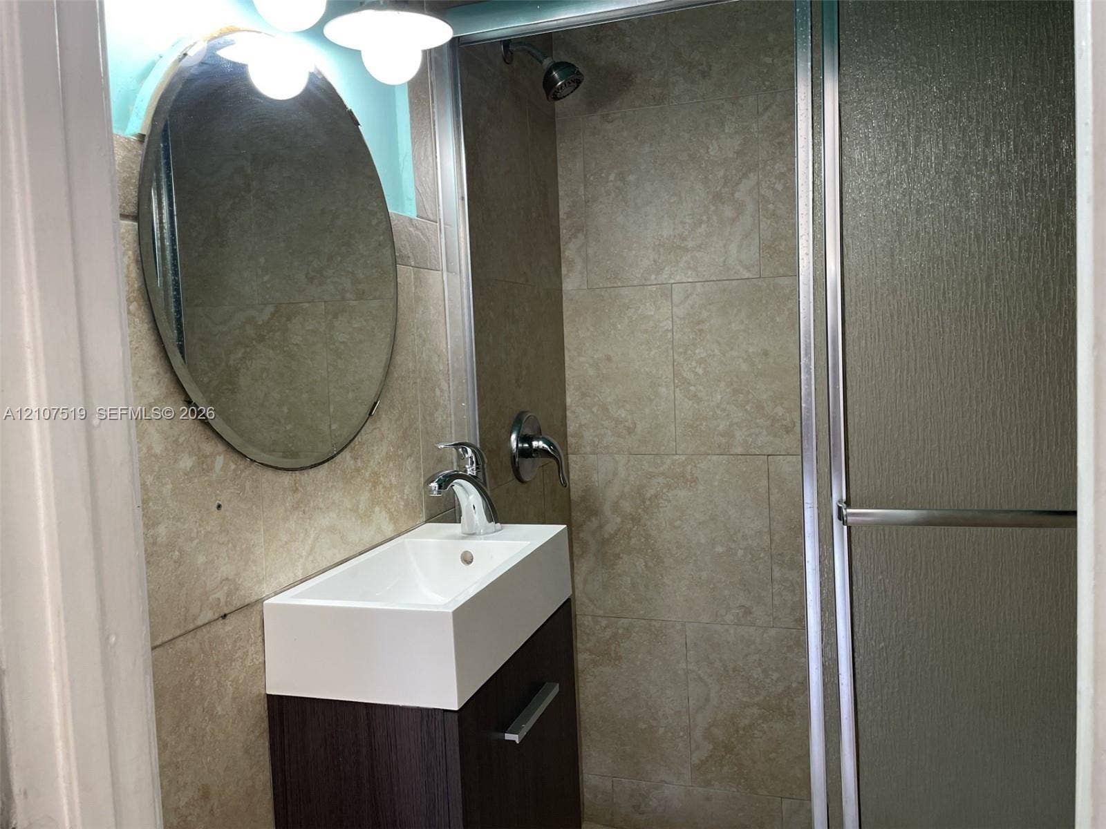 1201 SW 13th Street, #1205, Miami, Miami, FL 33145 Bathroom featuring a floating vanity with a rectangular sink, stone-finish wall tile, an oval mirror, and a shower enclosure with a glass door