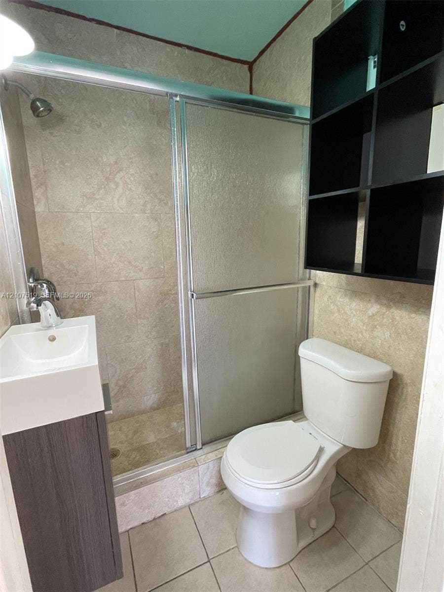 1201 SW 13th Street, #1205, Miami, Miami, FL 33145 Bathroom featuring a walk-in shower with sliding glass doors, stone-tiled shower surround, wall-mounted black cabinetry, and a vanity with an integrated sink