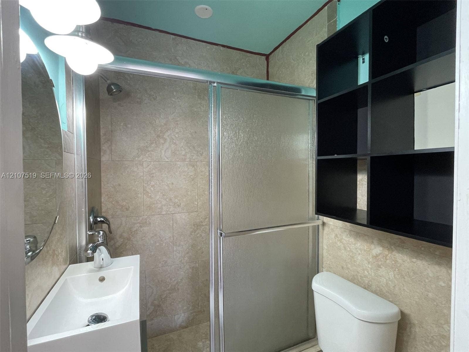 1201 SW 13th Street, #1205, Miami, Miami, FL 33145 Bathroom featuring full-height stone-finish tile surround, sliding glass shower door, wall-mounted black shelving, and white pedestal sink with chrome faucet