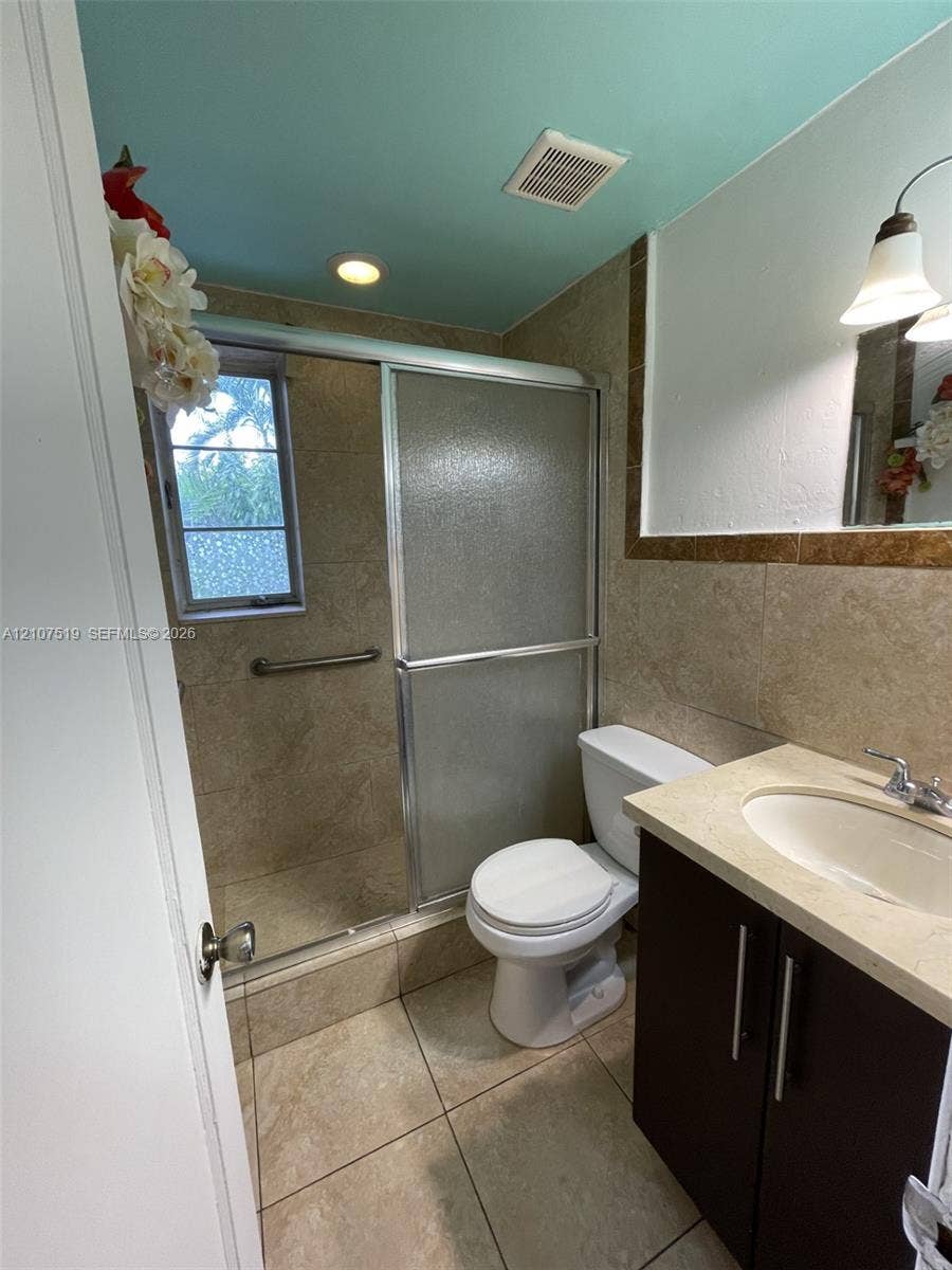 1201 SW 13th Street, #1205, Miami, Miami, FL 33145 Bathroom featuring large-format stone-finish floor and wall tiles, dark wood-finish vanity with an integrated countertop, sliding glass shower enclosure, and a window with textured privacy glass