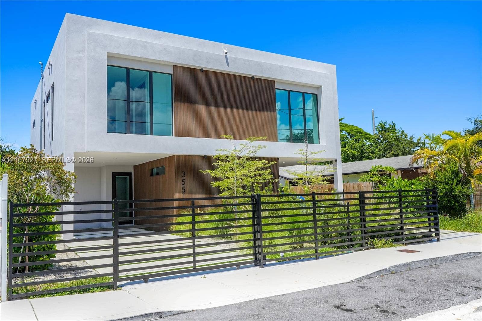 355 NW 50th Street, Miami, FL 33127 Contemporary two-story exterior featuring smooth stucco siding, wood-finish paneling, large-format glass windows, and a metal horizontal-slat security gate