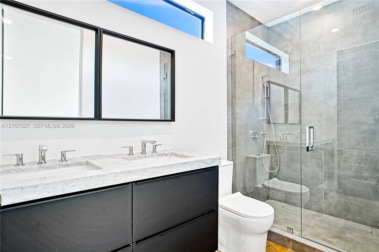 355 NW 50th Street, Miami, FL 33127 Floating vanity featuring a dual-sink stone countertop, walk-in shower with floor-to-ceiling tile, frameless glass enclosure, and transom windows