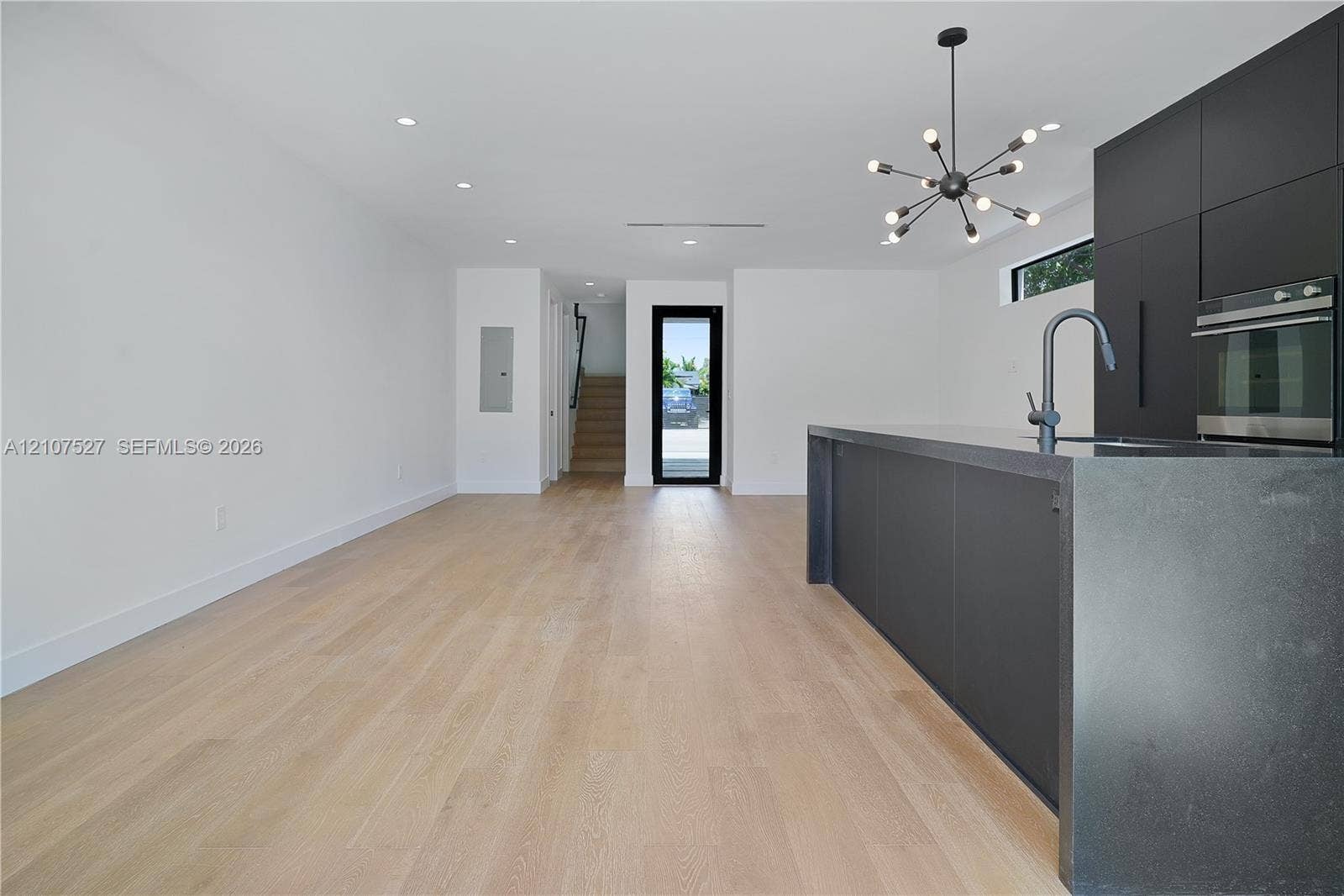 355 NW 50th Street, Miami, FL 33127 Modern kitchen featuring matte black flat-panel cabinetry, a dark waterfall-edge island, recessed lighting, a multi-light contemporary chandelier, and light-toned wood-finish flooring