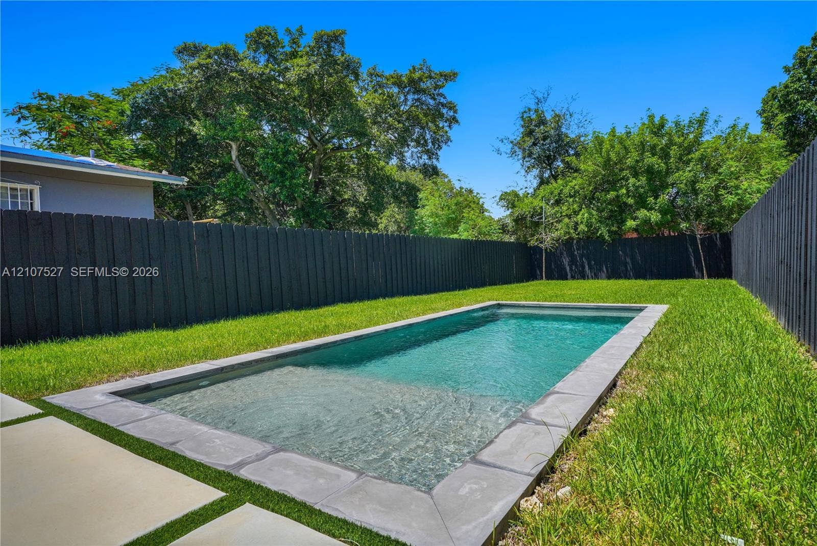 355 NW 50th Street, Miami, FL 33127 Rectangular swimming pool featuring stone coping, integrated shallow shelf, manicured lawn, and full-perimeter privacy fencing