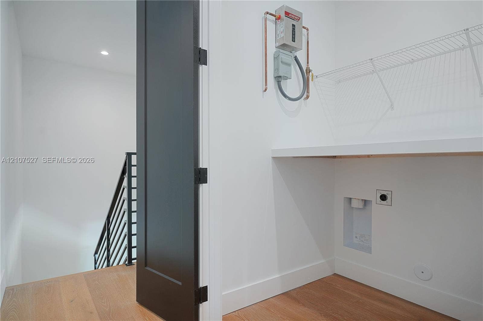 355 NW 50th Street, Miami, FL 33127 Utility space featuring wood-finish flooring, a wall-mounted tankless water heater, built-in shelving, and a solid-core dark finish interior door