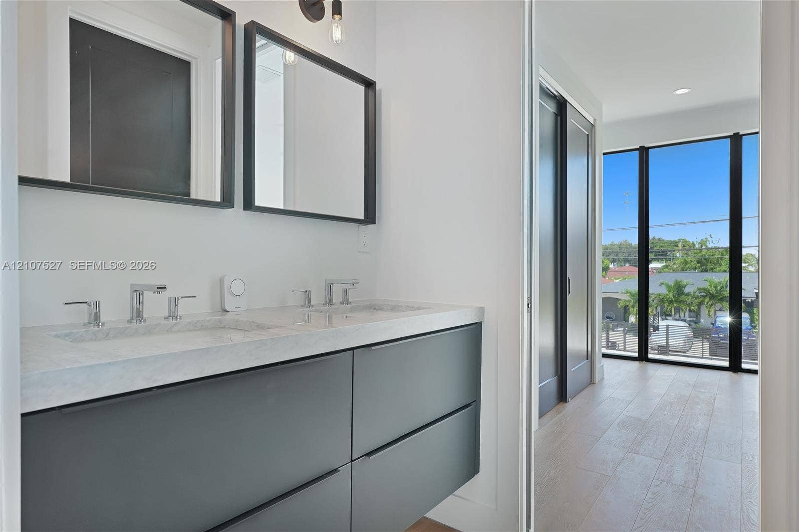 355 NW 50th Street, Miami, FL 33127 Floating vanity with dual-basin stone countertop, wall-mounted matte black-framed mirrors, wood-finish flooring, and floor-to-ceiling windows