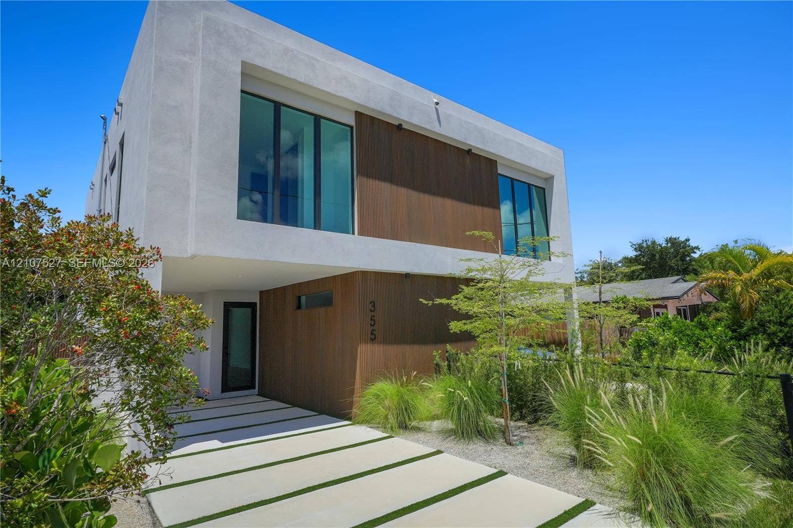 355 NW 50th Street, Miami, FL 33127 Modern two-story architectural exterior featuring smooth white stucco finish, vertical wood-finish siding, oversized floor-to-ceiling windows, and a segmented concrete paver driveway with integrated turf strips
