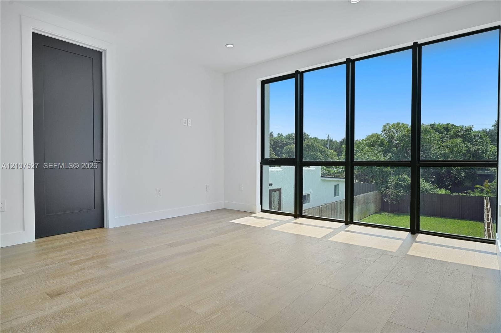 355 NW 50th Street, Miami, FL 33127 Floor-to-ceiling windows with black frames, wood-finish flooring, and a solid-core interior door with matte black hardware