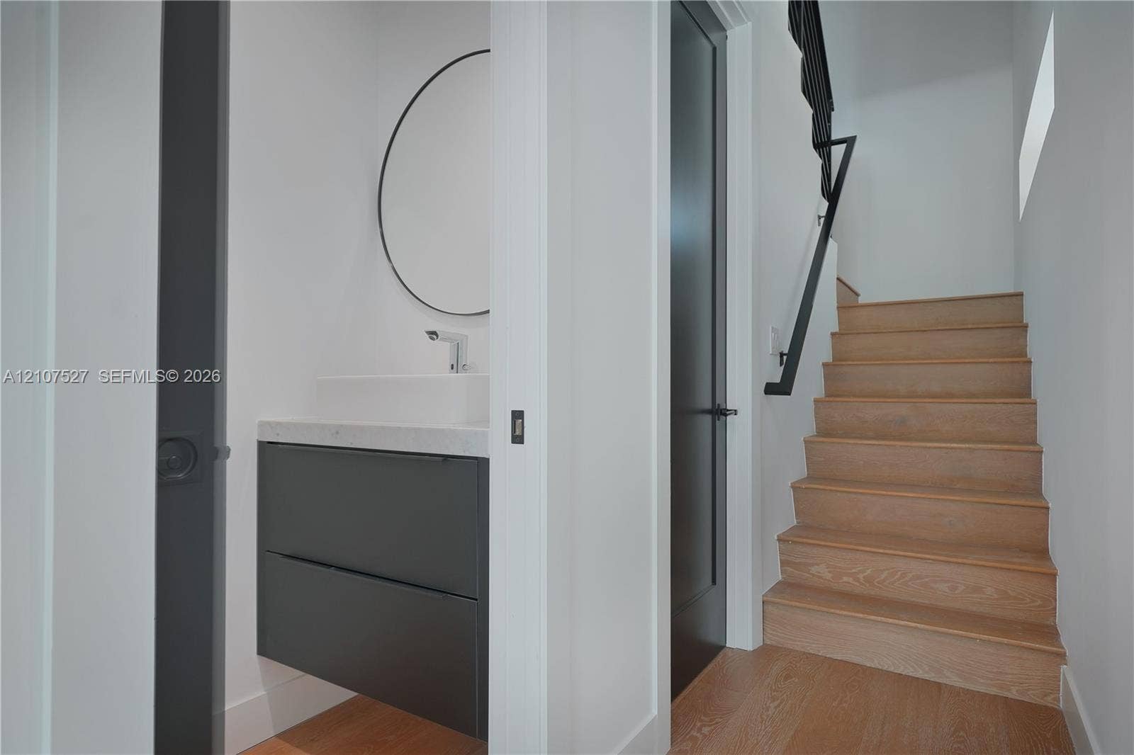 355 NW 50th Street, Miami, FL 33127 Floating vanity with stone countertop, circular wall-mounted mirror, wood-finish staircase with metal handrail, and solid-core doors
