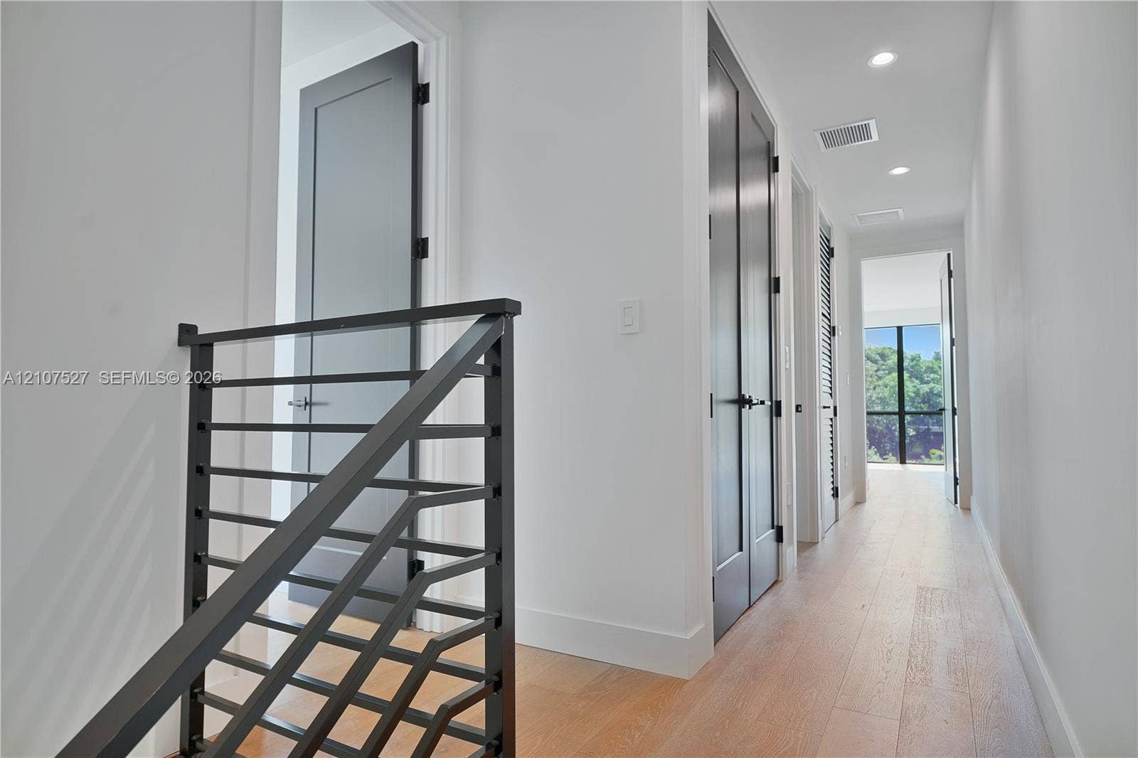 355 NW 50th Street, Miami, FL 33127 Hallway featuring wood-finish flooring, recessed lighting, matte black metal railing, and high-contrast dark-toned doors