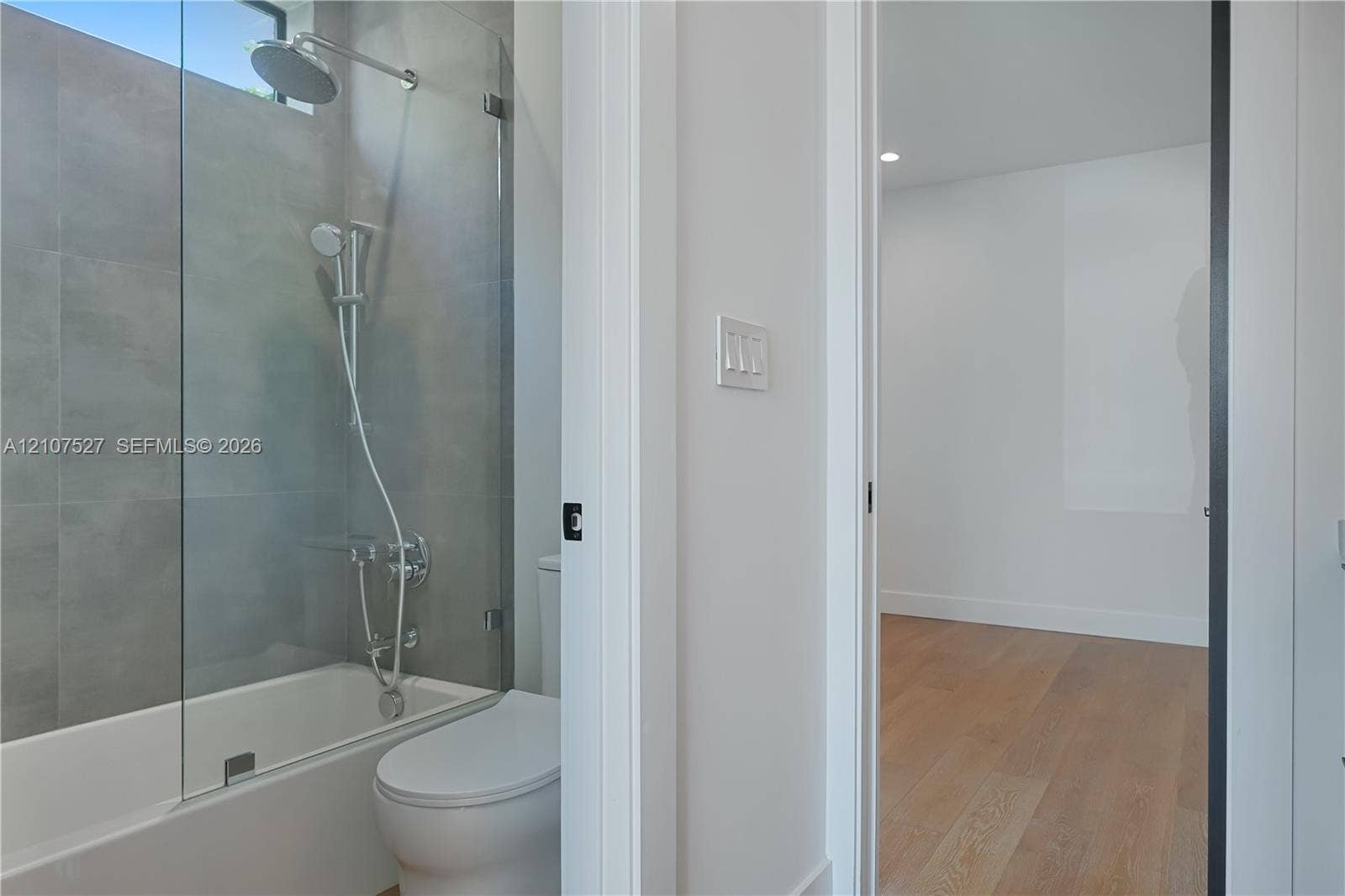 355 NW 50th Street, Miami, FL 33127 Bathroom featuring large-format grey tile surround, glass panel shower screen, rainfall shower head, and wood-finish flooring in the room beyond