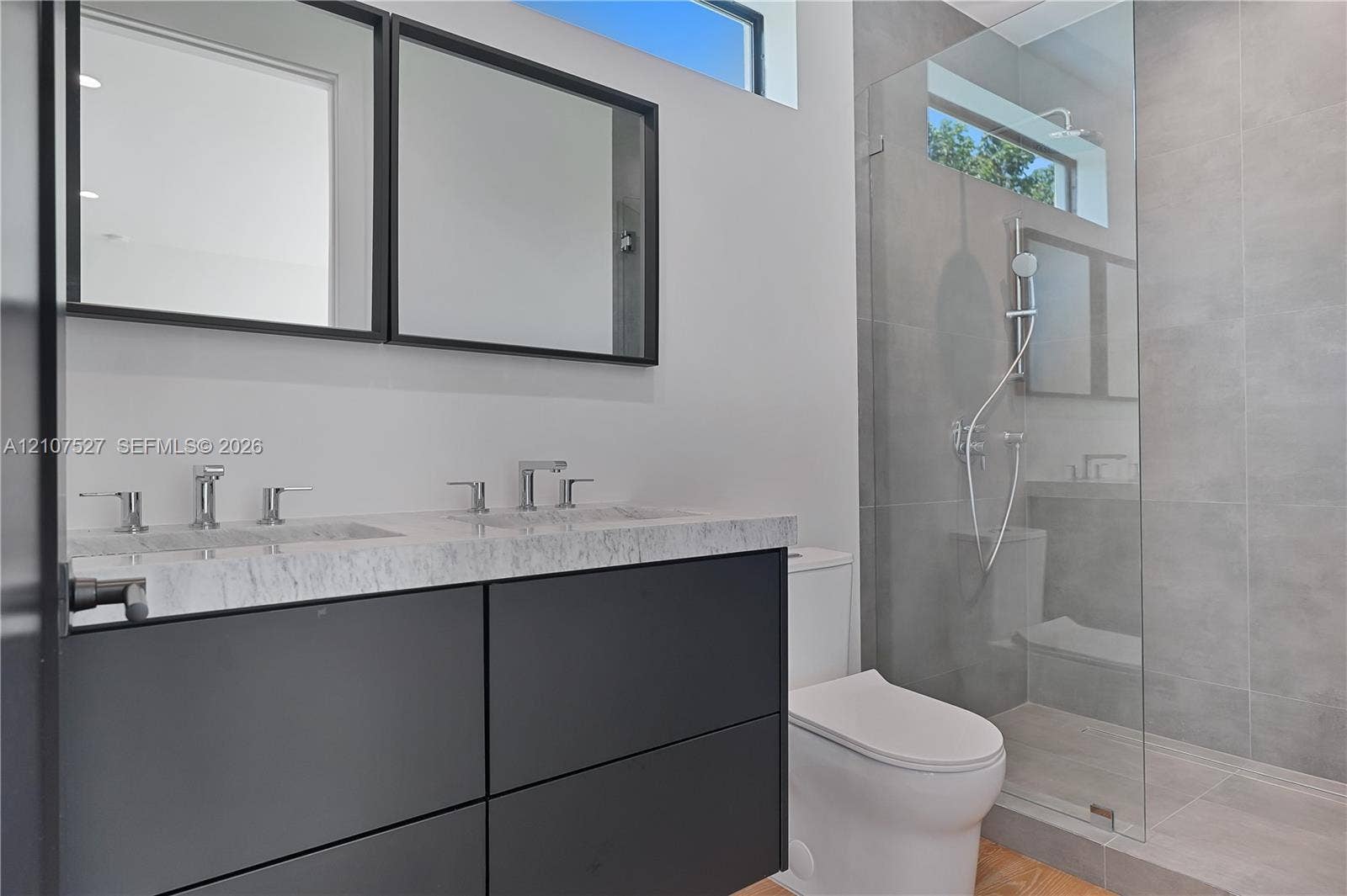 355 NW 50th Street, Miami, FL 33127 Floating dual-sink vanity with a stone countertop, framed mirrors, glass-enclosed shower with large-format tile, and rectangular transom windows