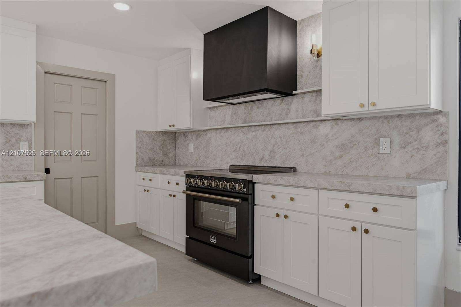 Kitchen featuring white shaker-style cabinetry, a large island with integrated microwave, stone-finish countertops and backsplash, black matte range with matching hood, and a multi-globe light fixture