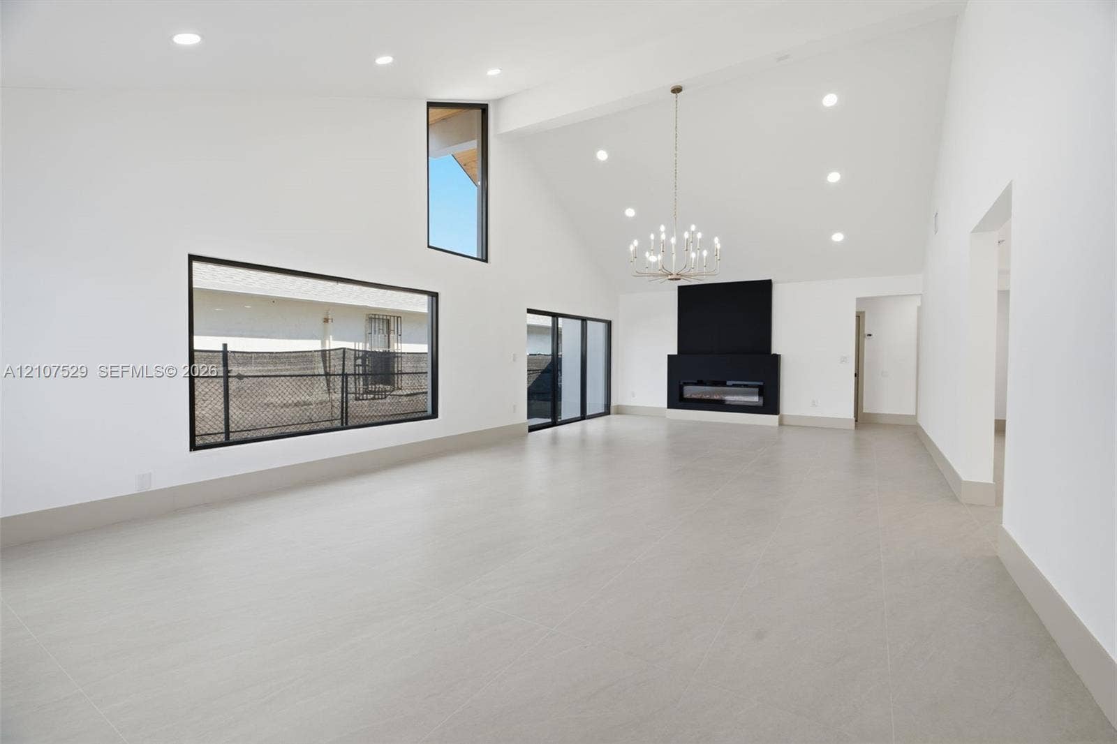 Vaulted ceilings featuring recessed lighting and a multi-tiered gold-tone chandelier, complemented by large-format neutral tile flooring and geometric paneled double entry doors