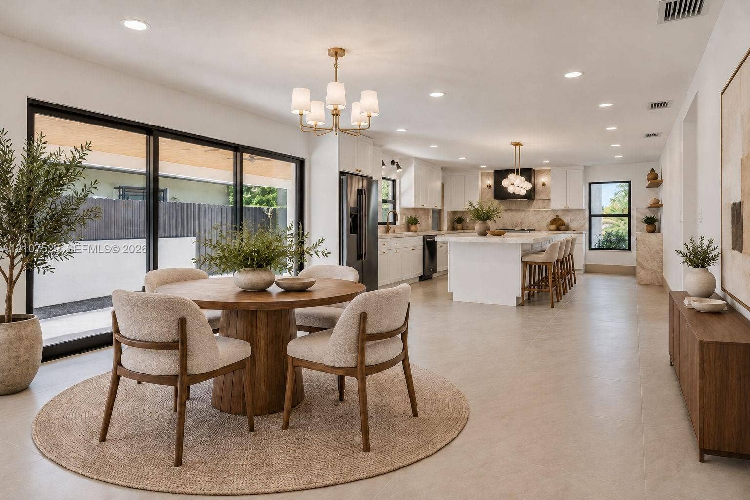 Open-concept interior featuring a center island with quartz countertops, custom white cabinetry, recessed lighting, multi-arm chandeliers, and large-format sliding glass doors