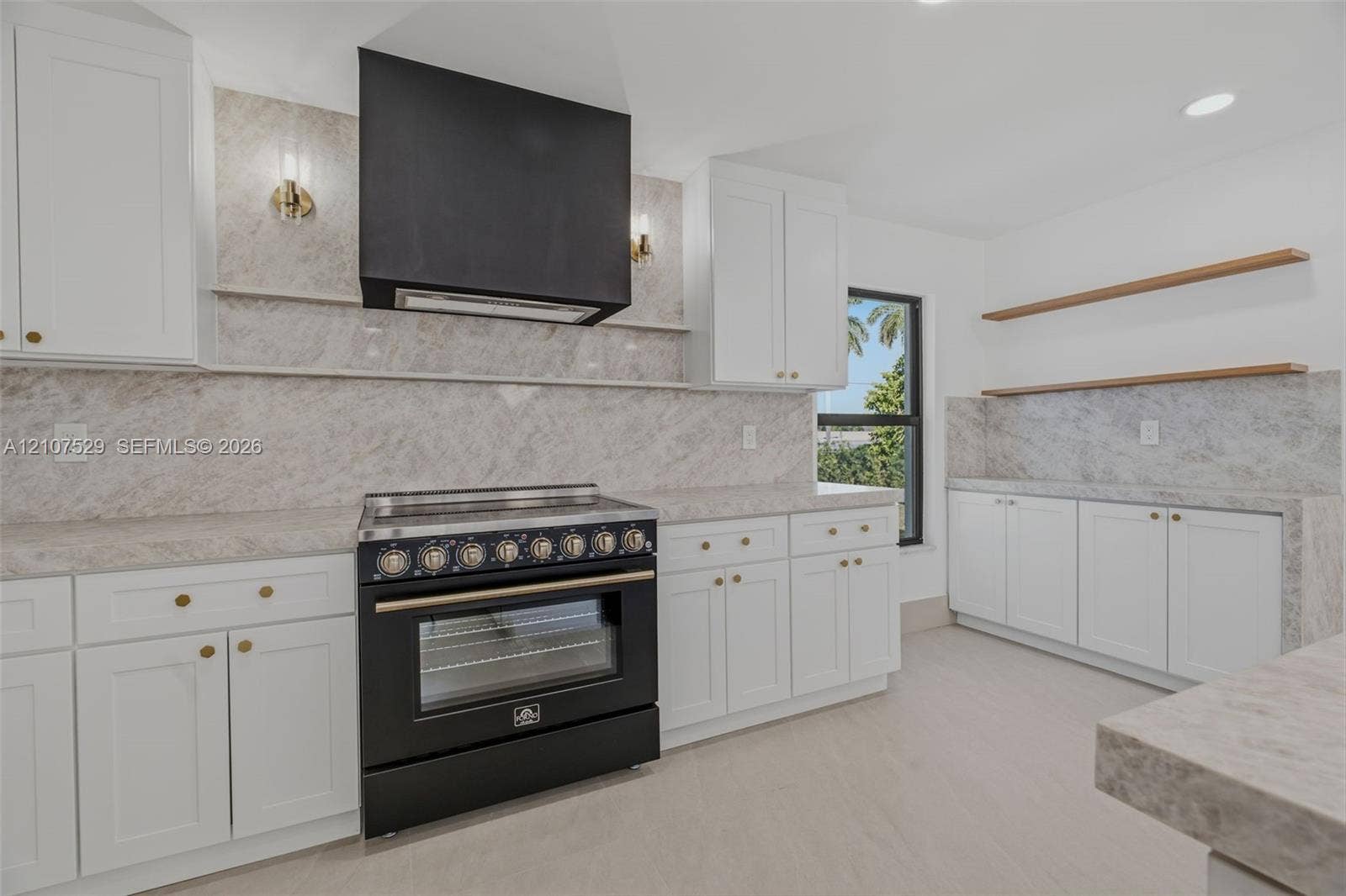 Kitchen featuring white shaker-style cabinetry, a contrasting matte black range hood, a dark finish freestanding range, and stone-surface countertops with matching full-height backsplash