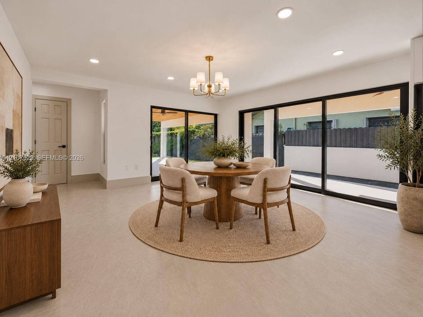 Neutral-toned interior featuring large-format flooring, recessed lighting, a multi-arm chandelier, and expansive sliding glass doors