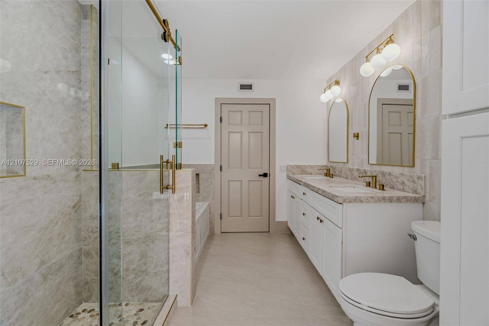 Walk-in shower with frameless glass enclosure, gold-toned hardware, stone-tile surround, and recessed wall niche, featuring a separate white soaking tub with integrated faucet