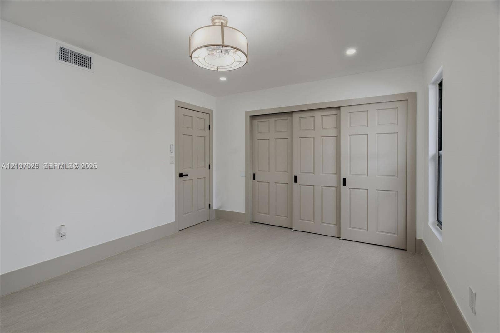 Neutral interior featuring large-format tile flooring, drum-style ceiling light fixture, recessed lighting, and windows with black frames