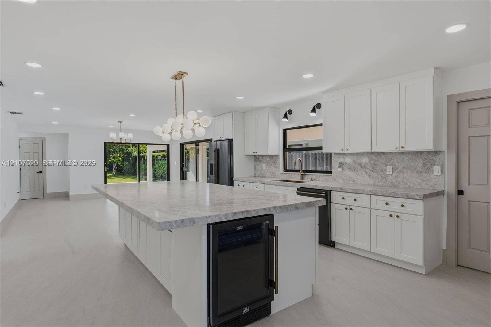 Large kitchen island with a stone-surface countertop, white Shaker-style cabinetry, matte gold-finish hardware, built-in microwave oven, and a contemporary multi-globe linear chandelier