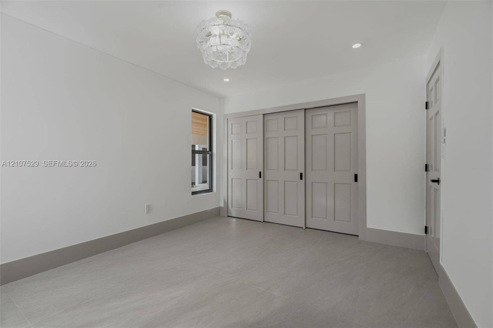 White shaker-style cabinetry with brass-tone hardware, stone-finish countertop, neutral large-format flooring, and drum-style ceiling fixture