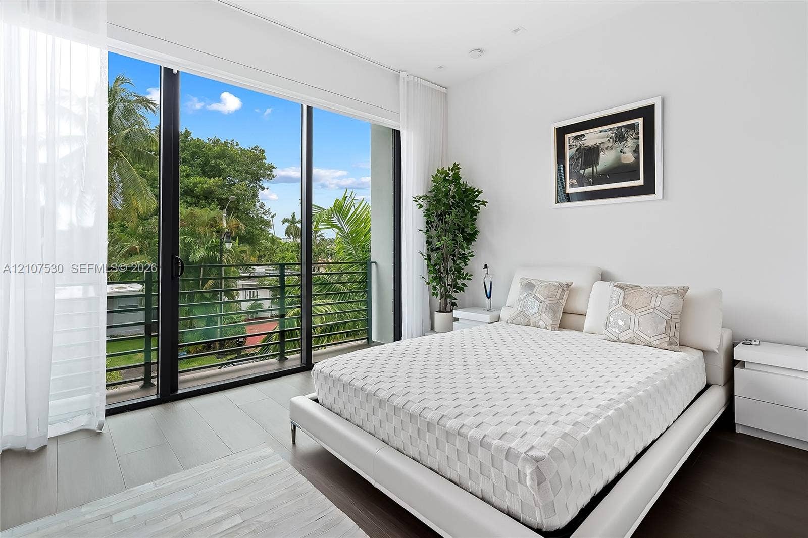 Floor-to-ceiling glass sliding doors opening to a balcony with metal railings and expansive exterior greenery