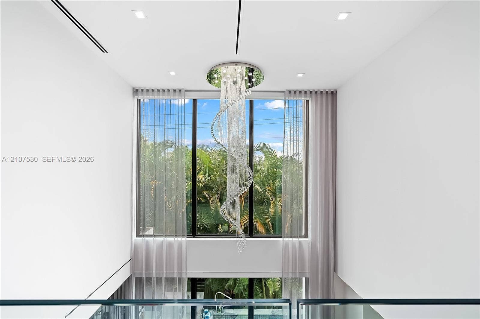 Floor-to-ceiling windows featuring a spiral crystal chandelier, recessed ceiling lighting, and a glass panel railing