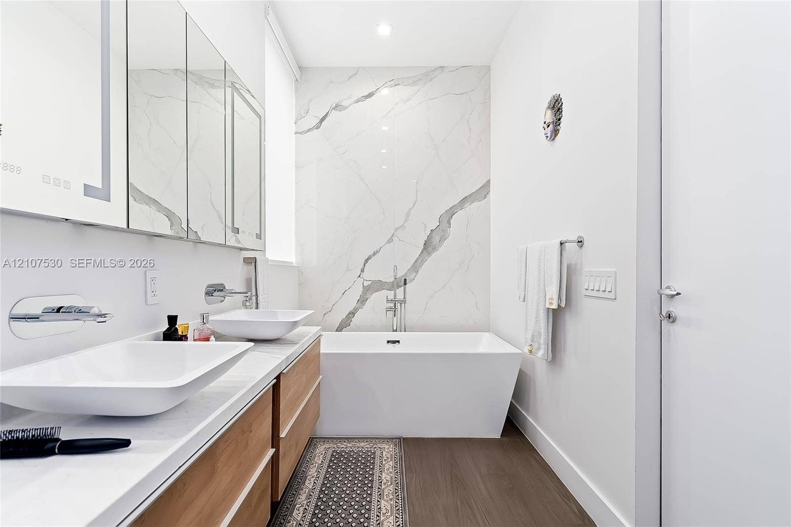 Floating double vanity with vessel sinks, wall-mounted faucets, large-format stone-finish wall paneling, and a freestanding soaking tub
