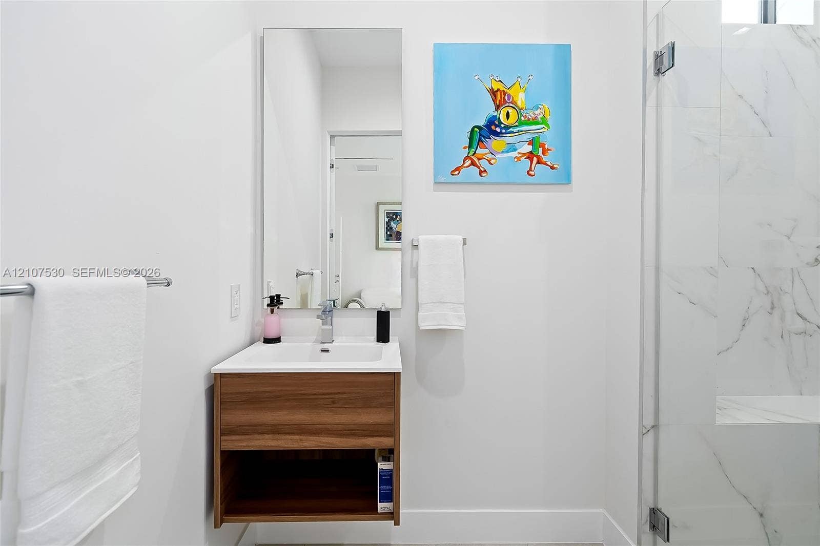 Floating wood-finish vanity with a rectangular sink, wall-mounted mirror, brushed metal hardware, and a glass-enclosed shower with stone-style wall tile