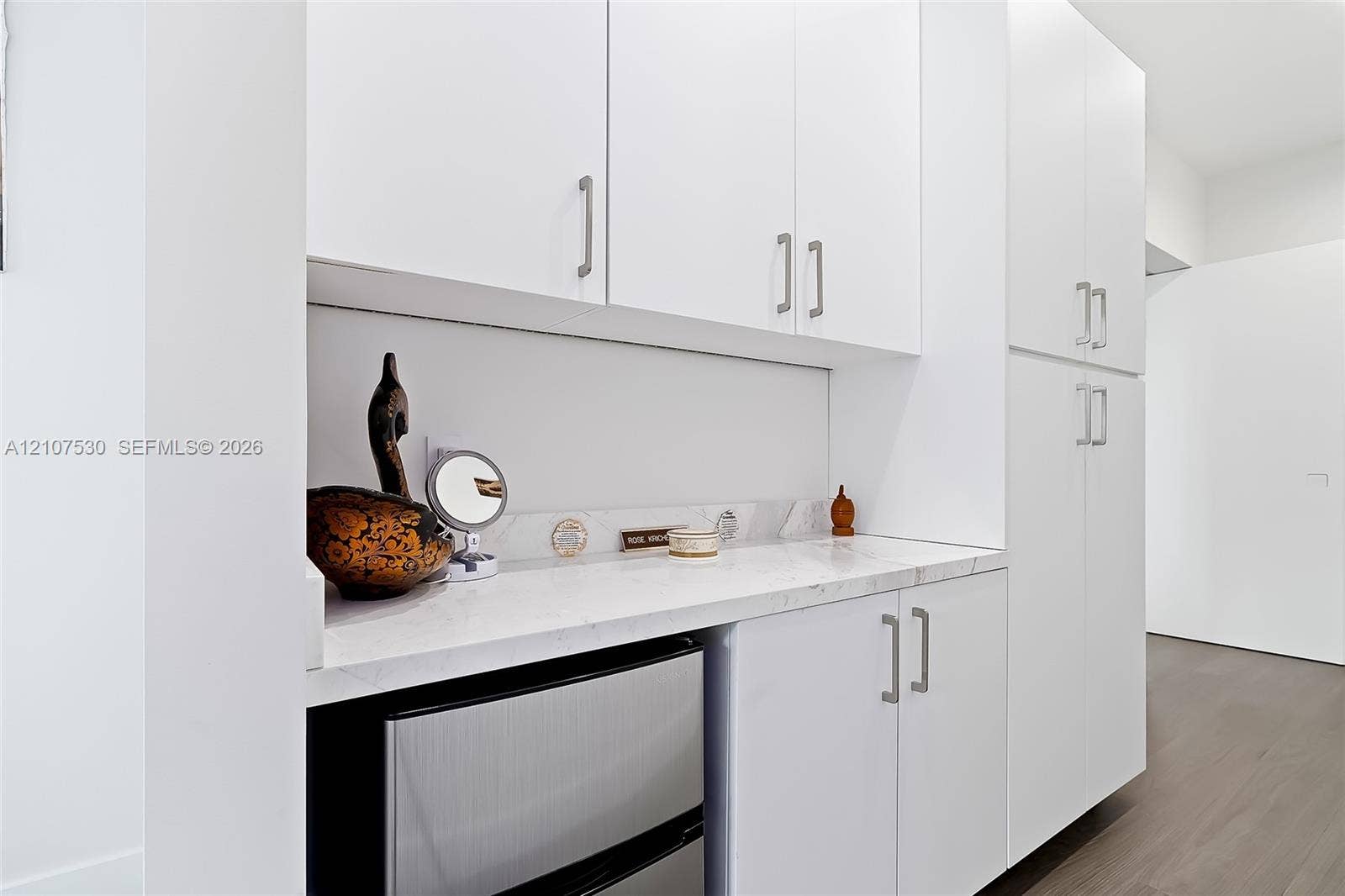 Custom cabinetry with white finish, integrated stone-surface countertop, matte metal hardware, and wood-finish flooring
