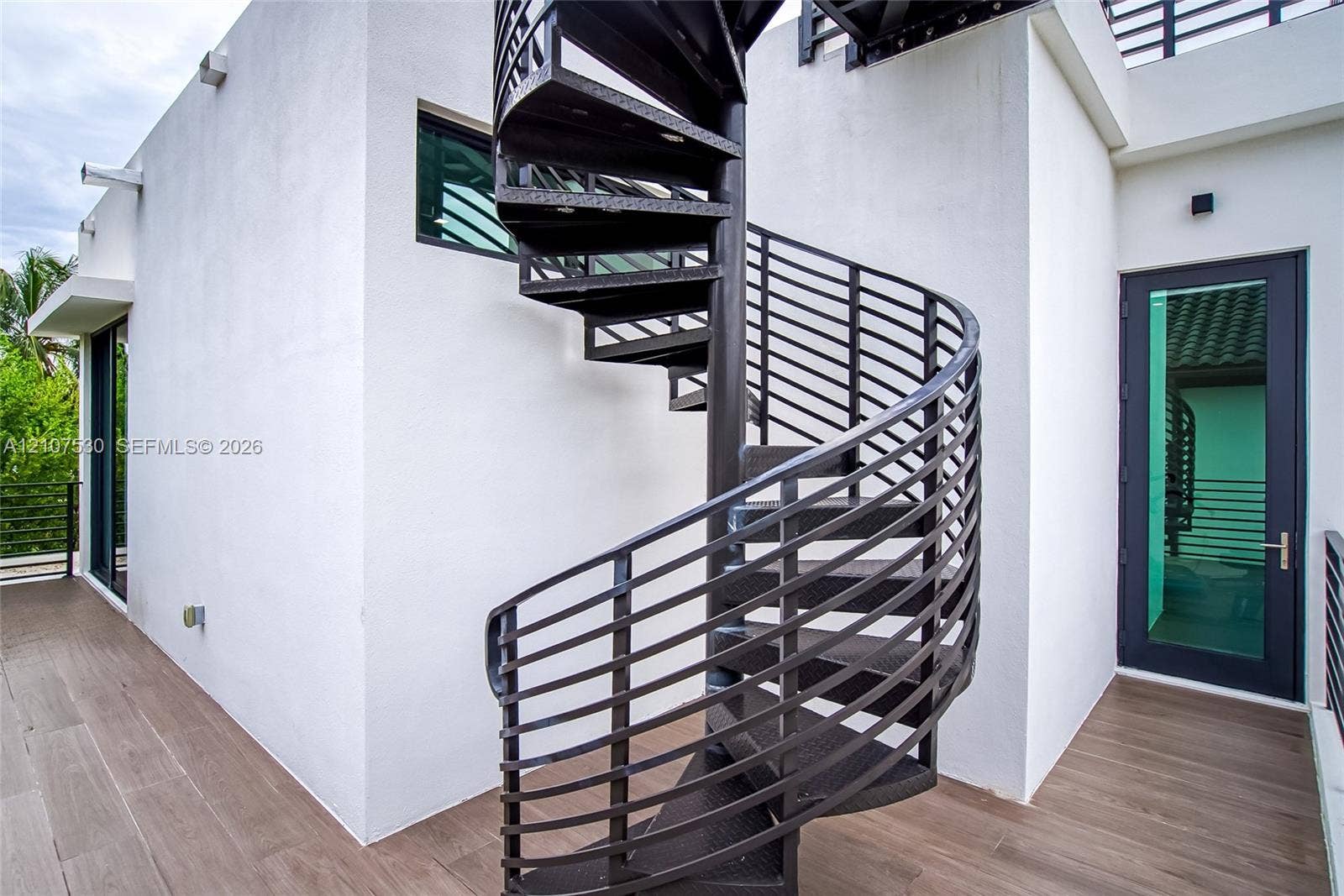 Black metal spiral staircase featuring open-riser treads, wood-finish flooring, and a glass-paneled entry door