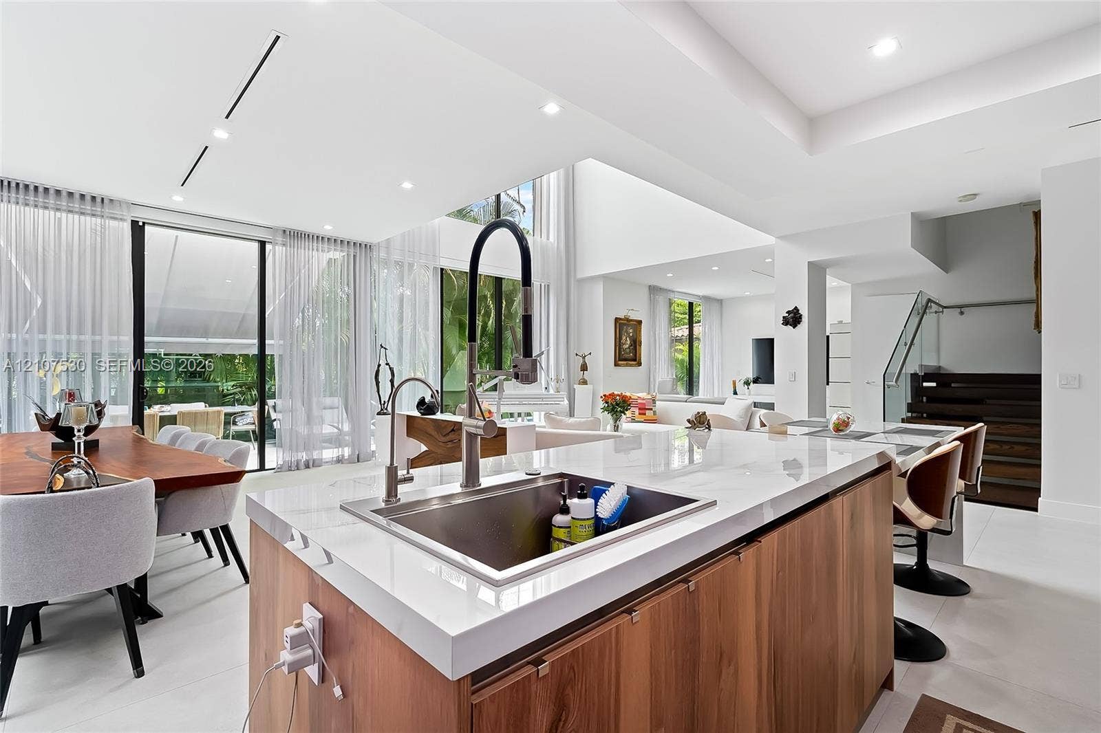 Kitchen island featuring light stone countertops, wood-finish cabinetry, a stainless steel undermount sink, and a high-arch pull-down faucet