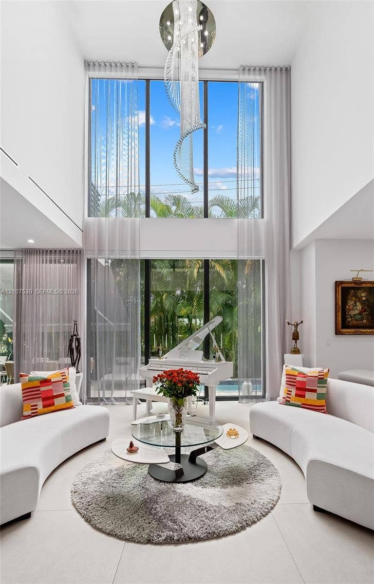 Double-height living area featuring floor-to-ceiling glass windows, a statement modern chandelier, and large-format tile flooring