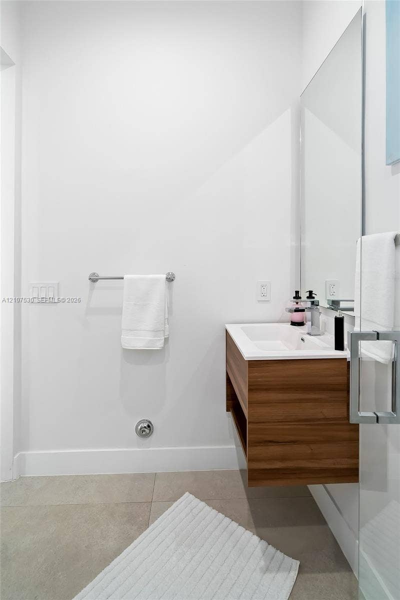 Wall-mounted wood-finish floating vanity with an integrated rectangular sink, chrome single-handle faucet, and large-format tile flooring