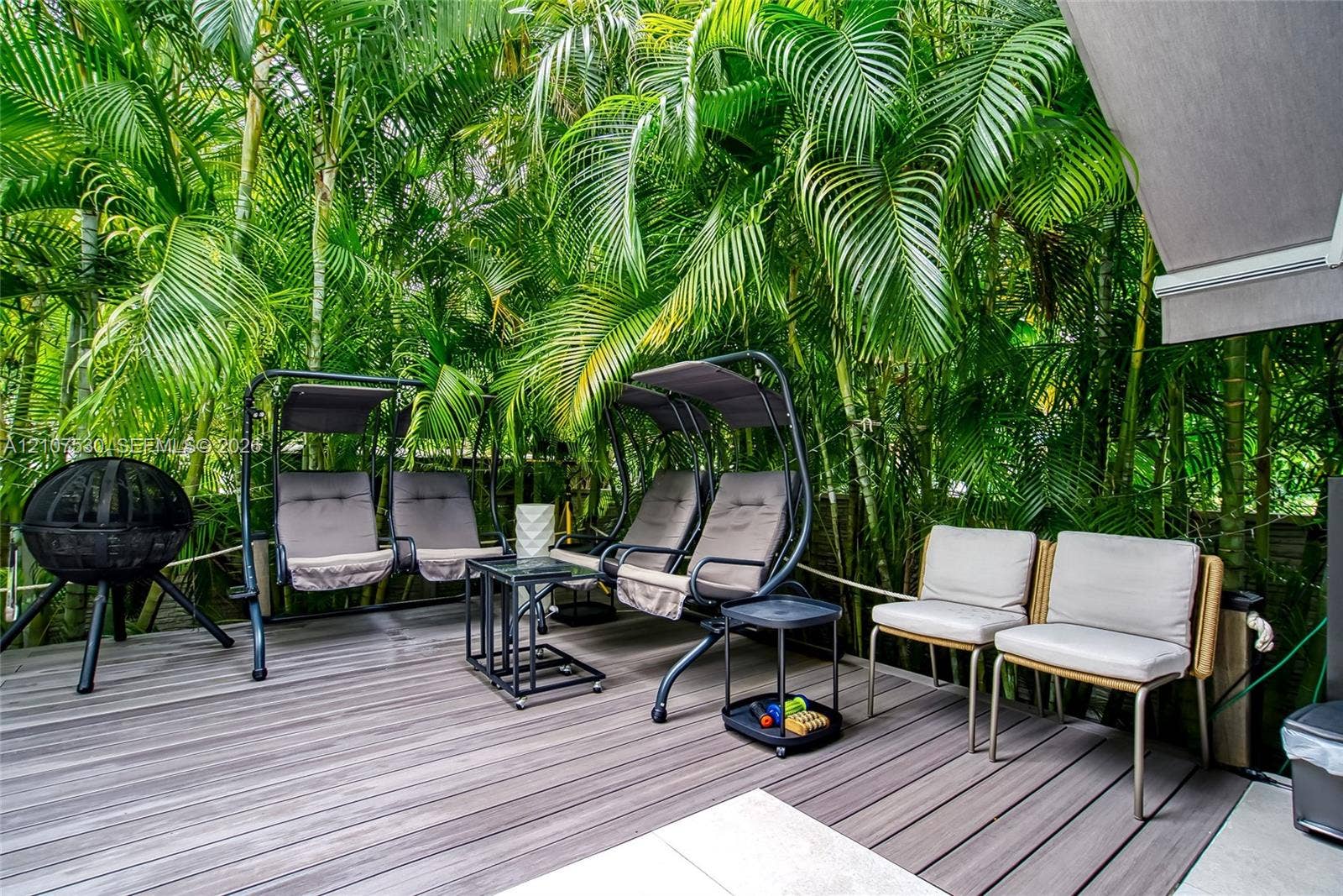 Composite wood-finish deck featuring a retractable awning and mature palm tree perimeter