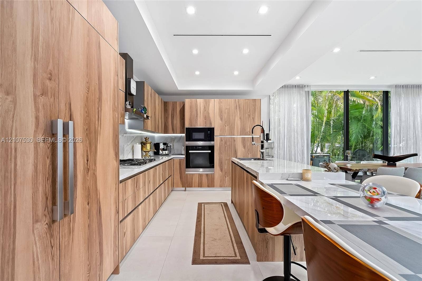 Kitchen featuring wood-finish cabinetry, stone countertops, integrated stainless steel appliances, a central island, and recessed ceiling lighting