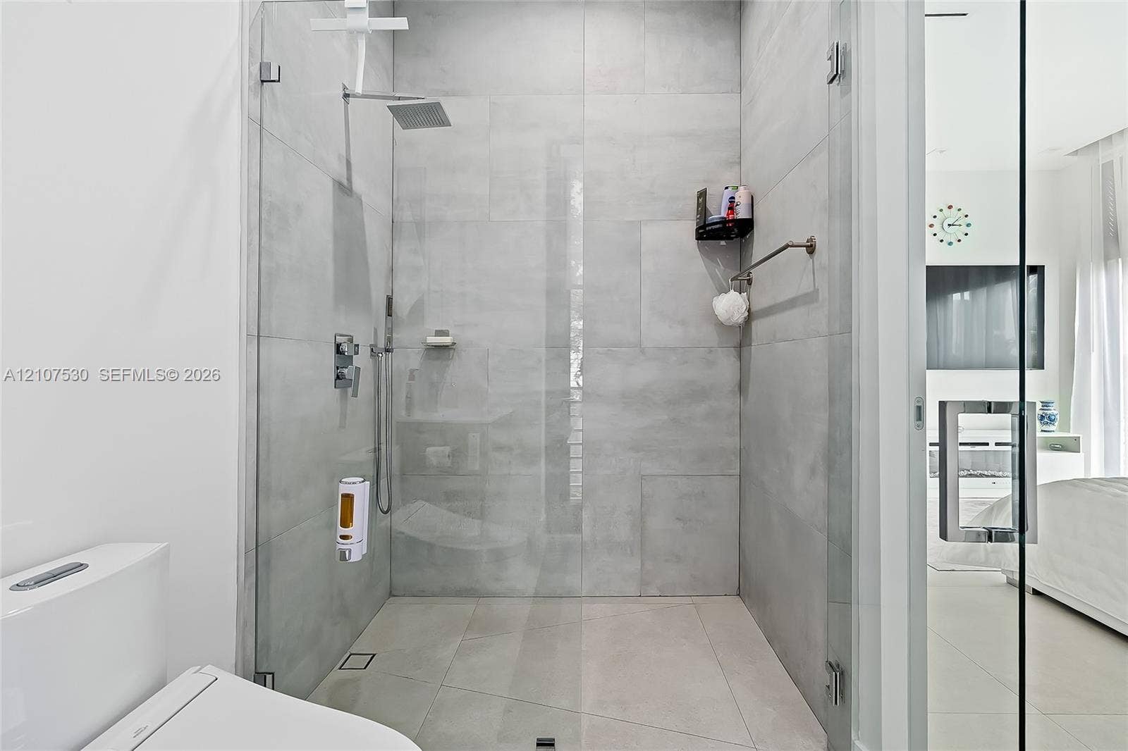 Walk-in shower featuring large-format grey tile, a frameless glass enclosure, a rainfall showerhead, and a wall-mounted chrome fixture set