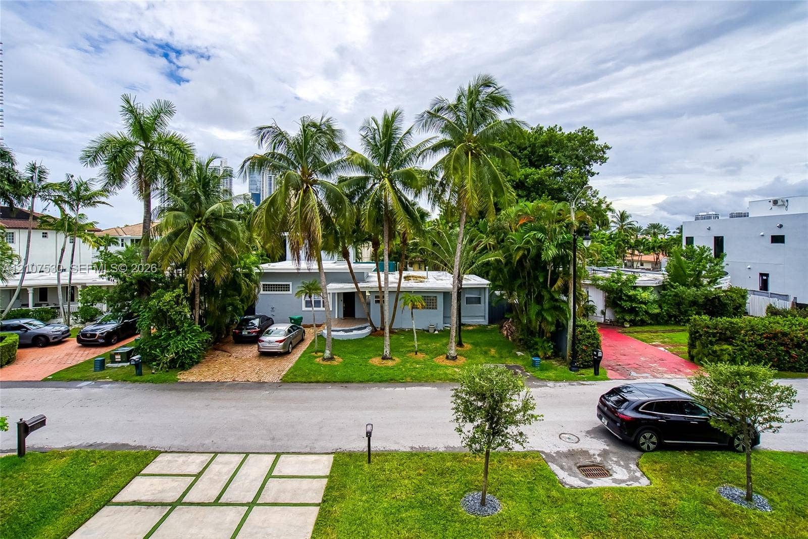Single-story residence featuring a paved brick driveway, low-profile flat roof architecture, established palm trees, and manicured landscaping