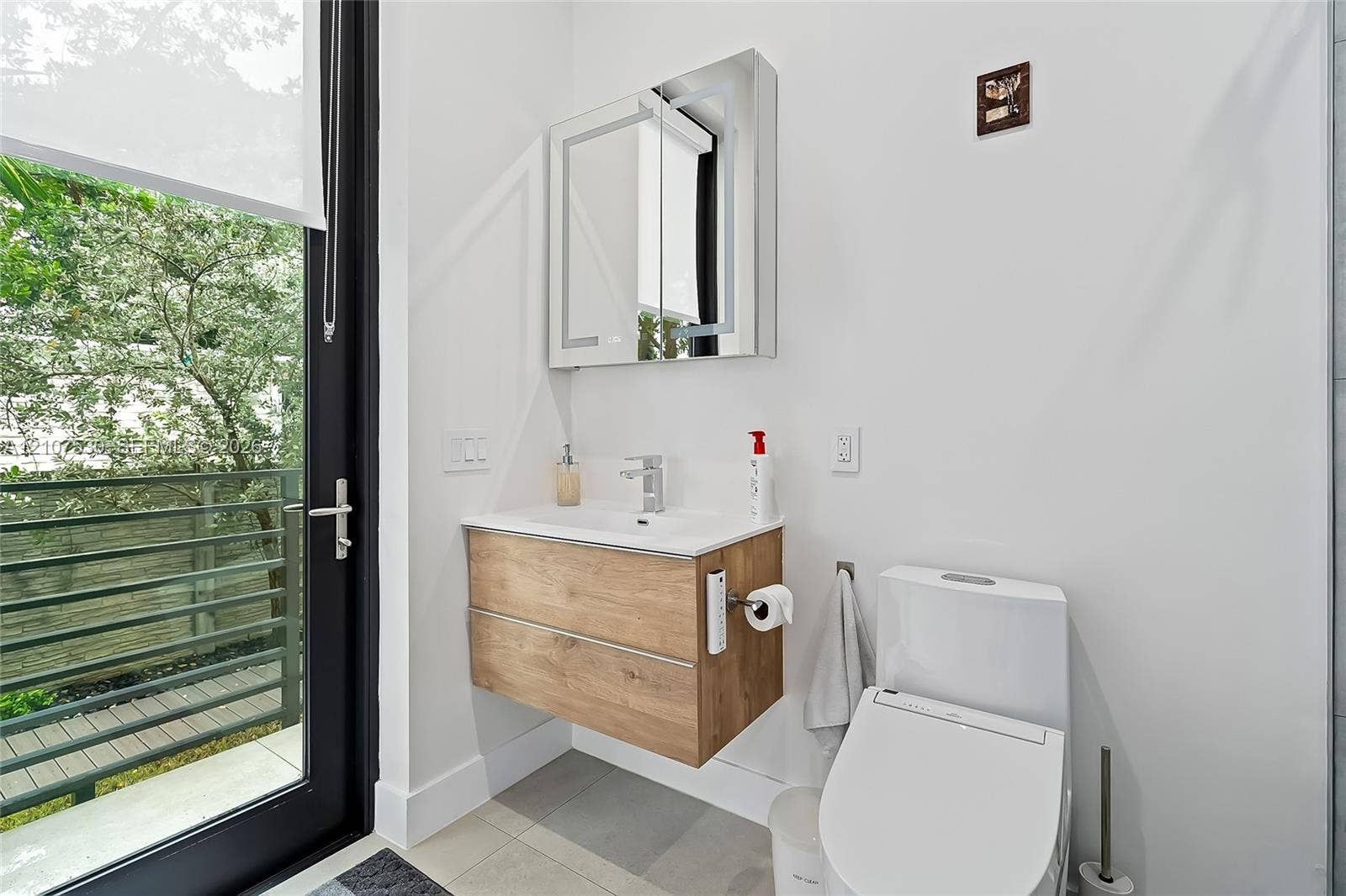 Wall-mounted vanity featuring wood-finish cabinetry and a white integrated sink, paired with a modern mirror-front medicine cabinet, polished chrome faucet, and low-profile toilet
