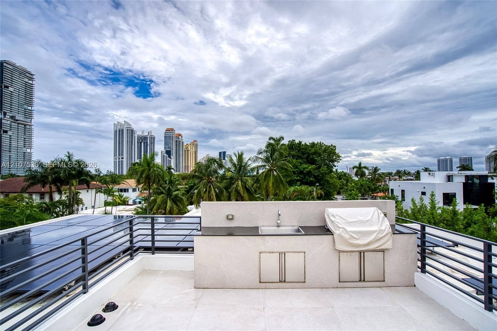 Rooftop terrace featuring large-format tile flooring, a built-in outdoor kitchen with a stainless steel sink, dark stone countertop, and black metal railings