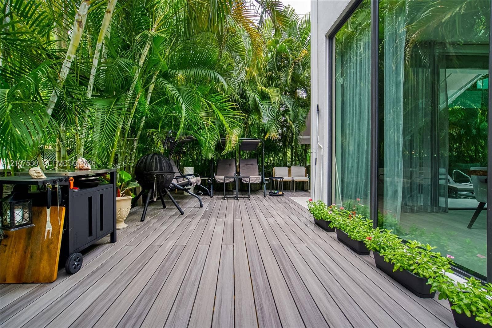 Outdoor composite decking featuring floor-to-ceiling glass paneling and privacy-enhancing mature palm landscaping