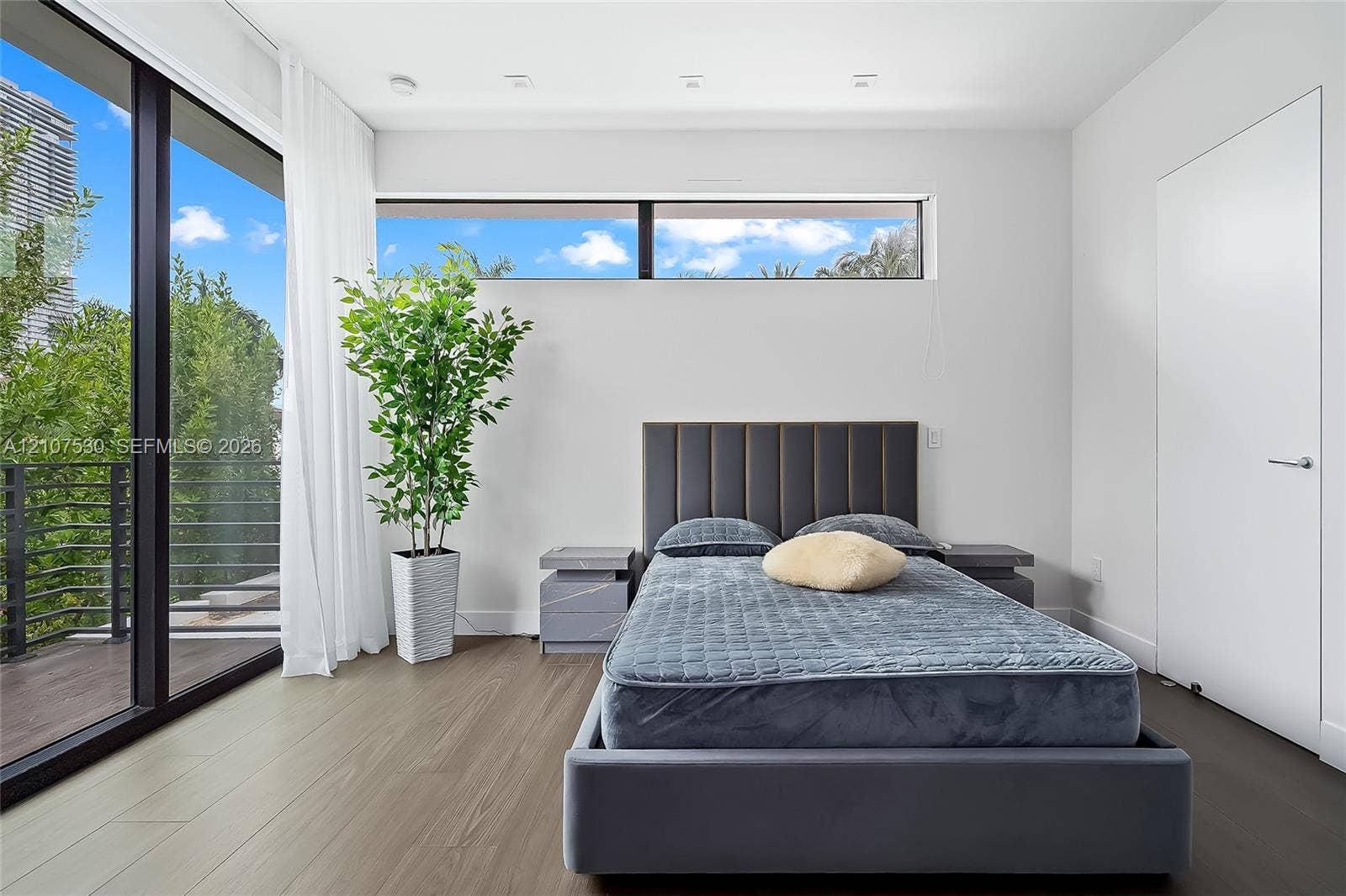 Floor-to-ceiling glass sliding doors, wood-finish flooring, recessed ceiling lighting, horizontal clerestory windows, and a private exterior balcony with metal railing