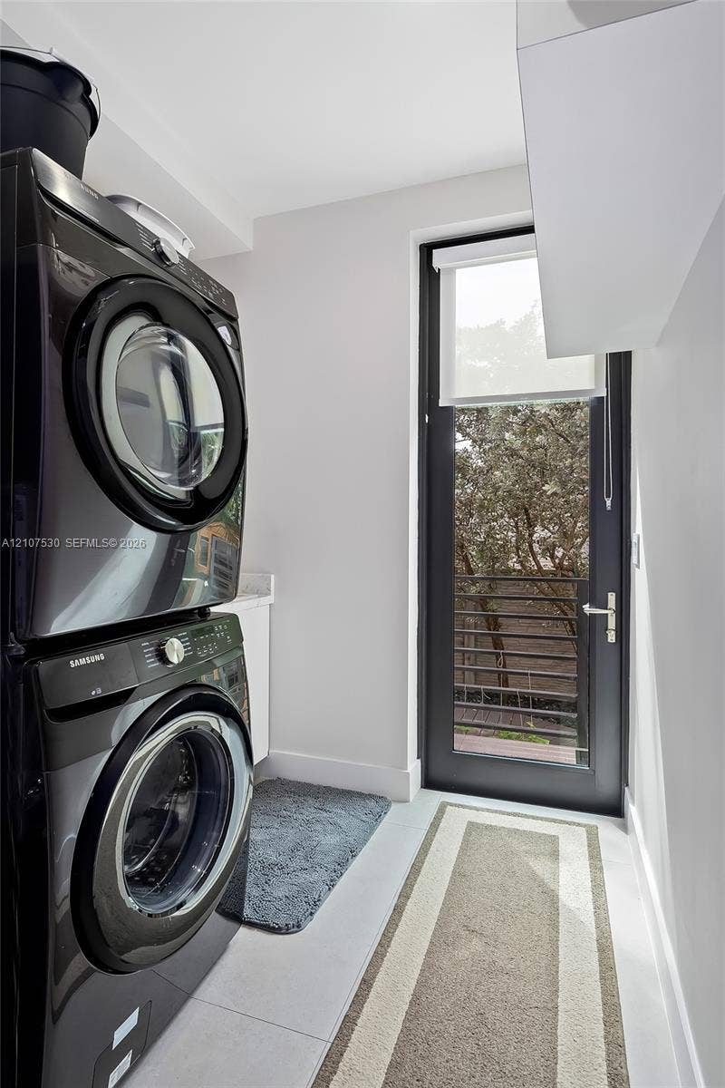 Laundry area featuring stacked appliances, a solid-surface countertop, cabinetry, and a full-height glass-panel door