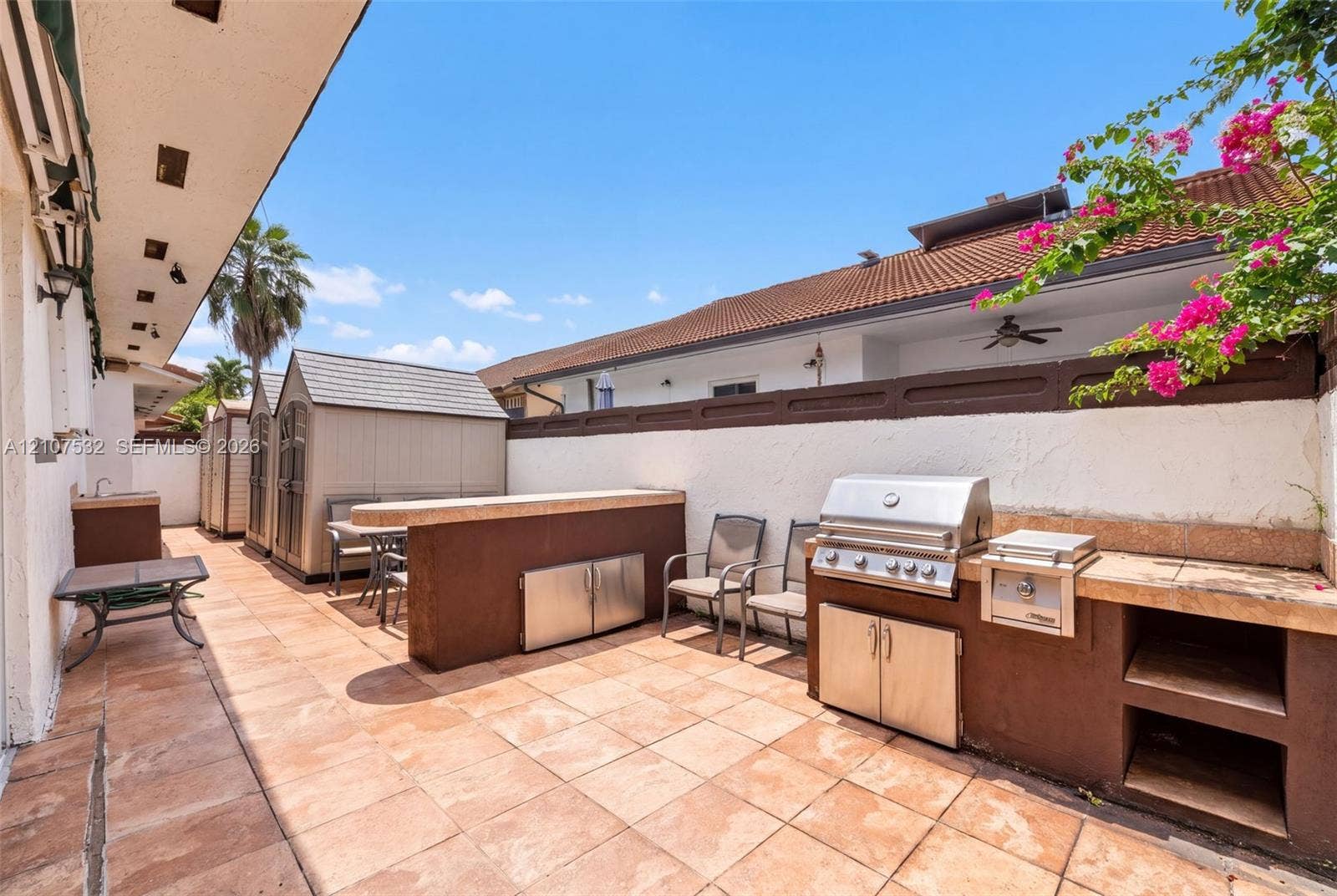 9124 NW 147th Terrace, Miami Lakes, FL 33018 Outdoor kitchen featuring a built-in stainless steel grill, stone-finish countertops, tiled patio flooring, and stucco wall enclosure