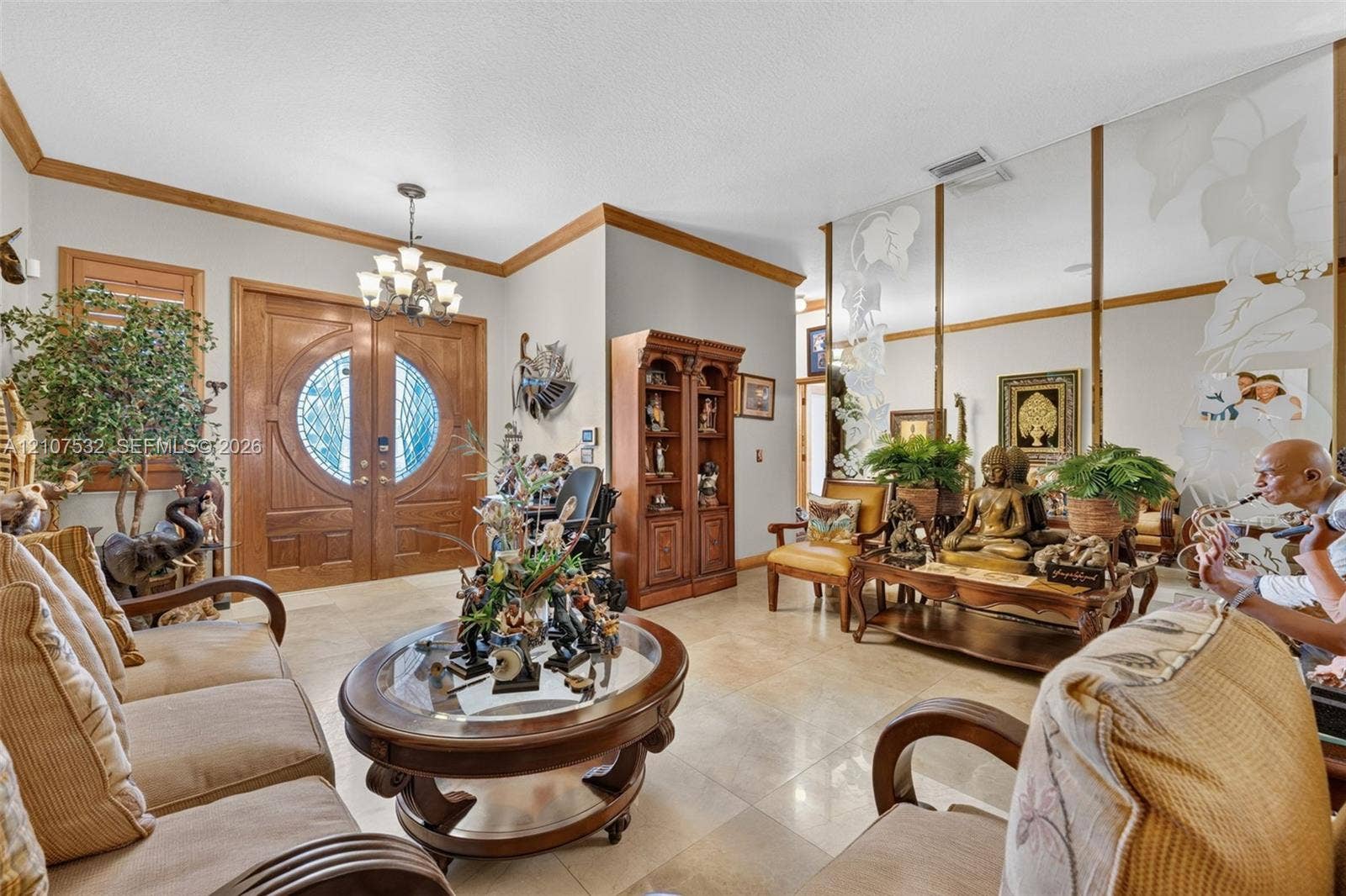 9124 NW 147th Terrace, Miami Lakes, FL 33018 Entryway featuring double wood doors with circular glass inserts, tile flooring, crown molding, a decorative multi-arm chandelier, and full-wall mirrored paneling