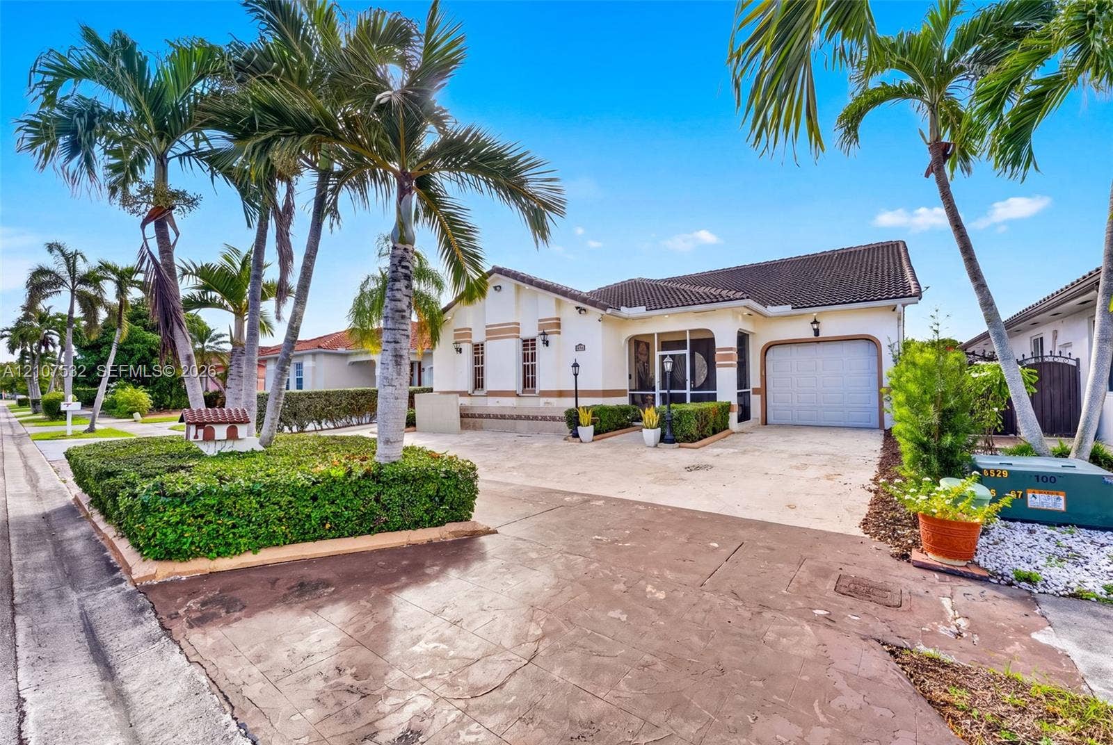 9124 NW 147th Terrace, Miami Lakes, FL 33018 Single-story exterior featuring a light-toned stucco faade, a tiled roof, an attached garage, and mature palm trees