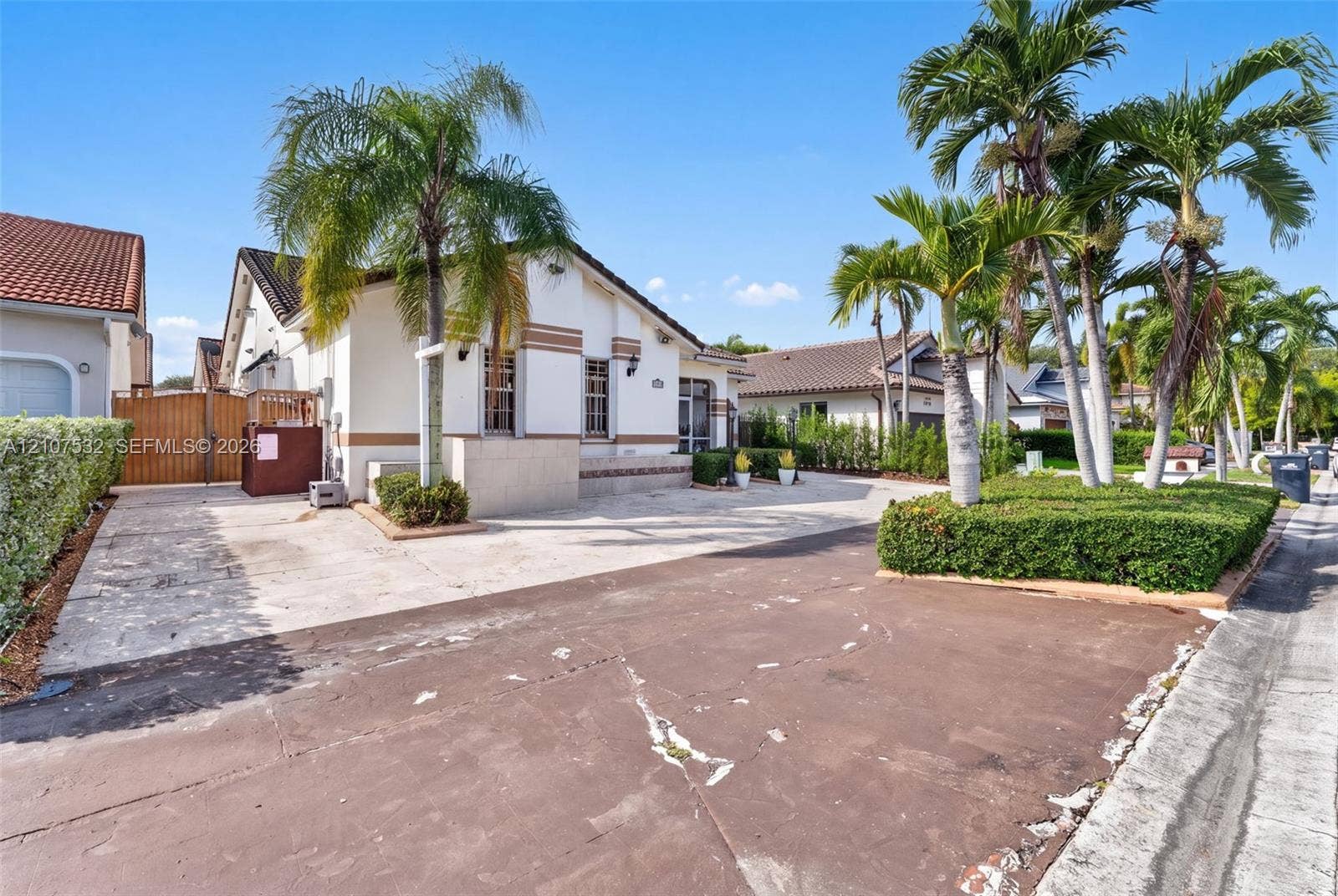 9124 NW 147th Terrace, Miami Lakes, FL 33018 Stucco exterior with horizontal detailing, concrete paved driveway, wood-finish privacy gate, and manicured palm tree landscaping