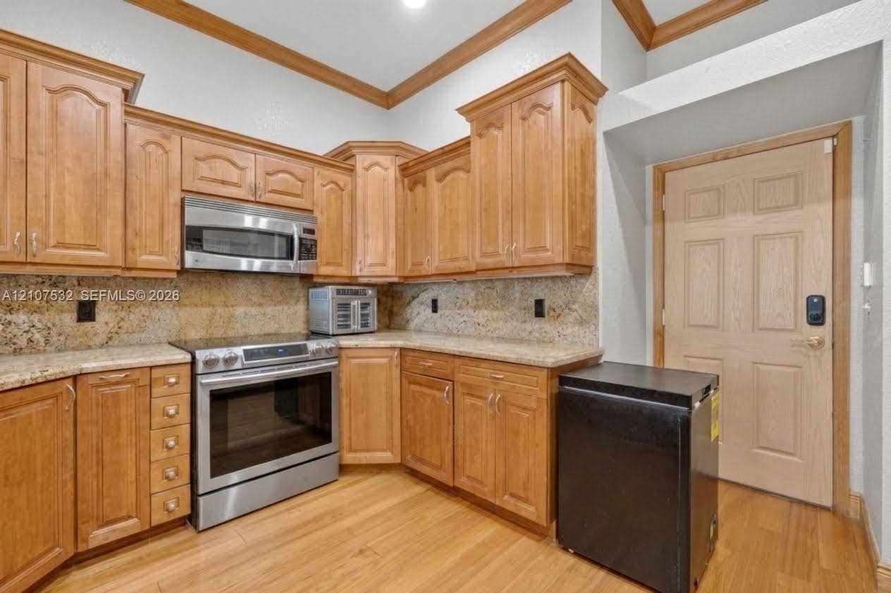 9124 NW 147th Terrace, Miami Lakes, FL 33018 Kitchen featuring natural finish wood cabinetry, stone countertops, stainless steel appliances, crown molding, and wood-finish flooring