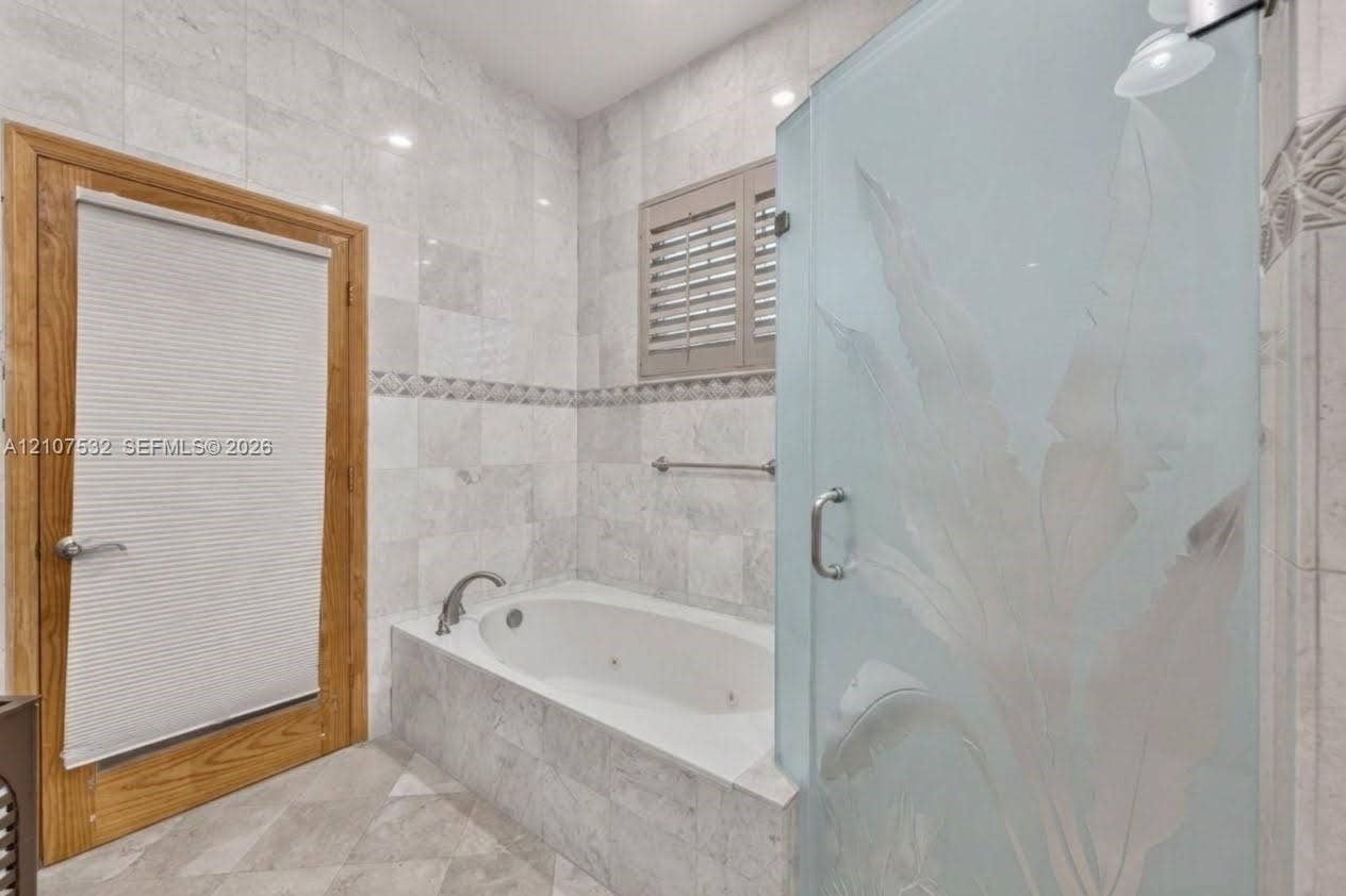 9124 NW 147th Terrace, Miami Lakes, FL 33018 Jetted soaking tub set in a tile-surrounded deck, walk-in shower with decorative etched-glass enclosure, natural stone wall tiling with an accent border, and wood-finish door trim